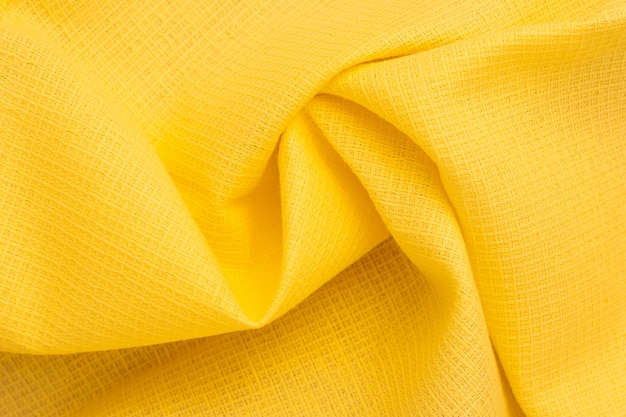 Abstrakter Hintergrund des hellen gelben Gewebes. Falten, Falten aus Baumwolltextil. Materialmuster, Stoffstruktur. Wellen auf Tapete.