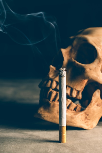 Abstrakter Stillleben-Schädel eines Skeletts mit brennender Zigarette, hören auf, Kampagne mit copyspace zu rauchen.