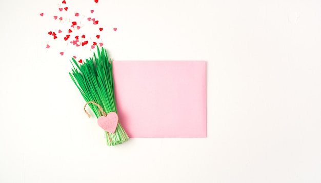 Abstrakter Strauß des Grases und der kleinen Herzen und einer rosa Hülle auf einem hellen Hintergrund.