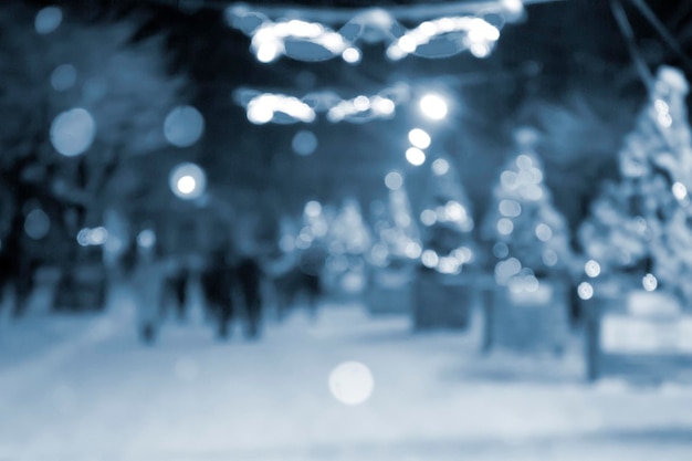 Abstrakter unscharfer Hintergrund Menschen, die auf der Straße von geschmückten Weihnachtsbäumen spazieren gehen, die leuchtend geschmückt sind