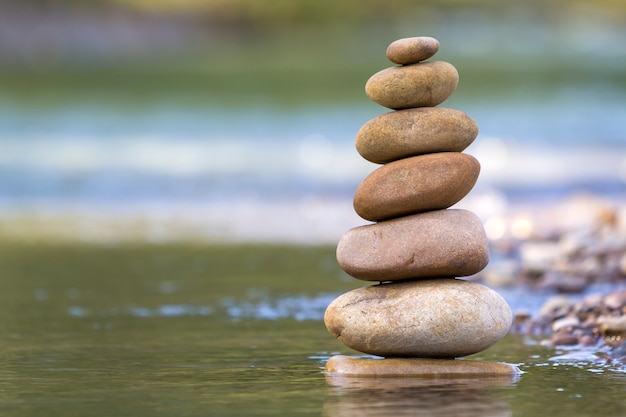 Abstraktes Bild der Nahaufnahme von nassen rauen natürlichen braunen ungleichen verschiedenen Größen und von Formsteinen balancierte wie Pyramidenstapelmarkstein im seichten Wasser