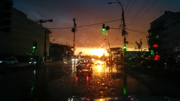 Abstraktes Bild durch nasse Autowindschutzscheibe auf movng Transport und Automobilen im Regen bei Sonnenuntergangsstrahlen