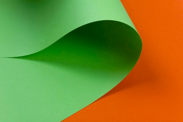 Abstraktes Design von grünem kurvenförmigen Papier auf orangefarbenem Hintergrund Kopierraum Flachlag