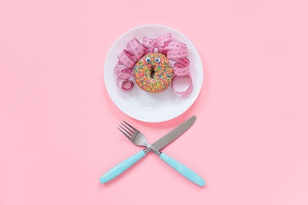 Abstraktes lustiges Gesicht der Frau vom Donut mit den Augen und dem Haar vom Zentimeterband auf Platte. Diät oder ungesundes Nahrungsmittelkonzept