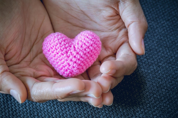 Abstraktes rotes und rosafarbenes Herz, das in der Hand für den Valentinstag gestrickt wird Liebeskonzept