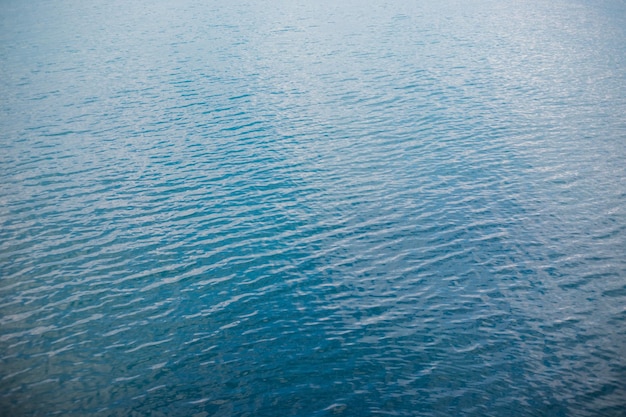 Abstraktion der Oberfläche des blauen Wassers, das vom Sonnenlicht als Hintergrund reflektiert wirdDraufsicht auf das Meerwasser Das Konzept der Entspannung am Strand UrlaubDie Textur der Wellen