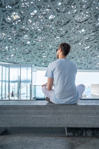 Abu Dhabi, Emiratos Árabes Unidos, 20 de mayo de 2020: Joven sentado en el Louvre en Abu Dhabi explorando el arte.