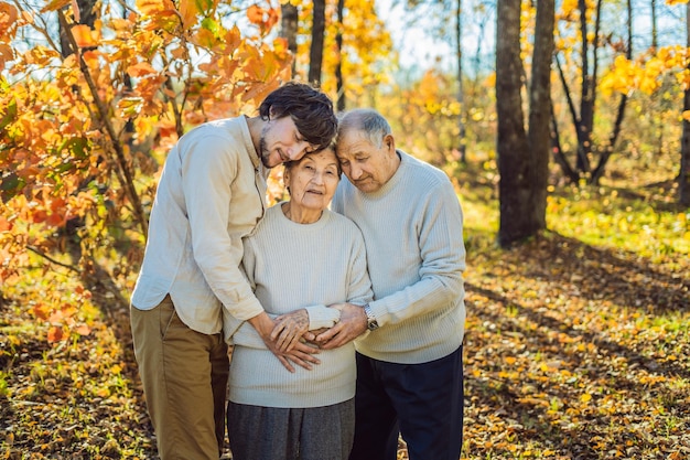 Abuela, abuelo y nieto adulto abrazándose en el parque de otoño