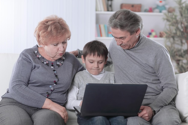 Abuela abuelo y nieto mirando la pantalla del portátil mientras se relaja en el sofá