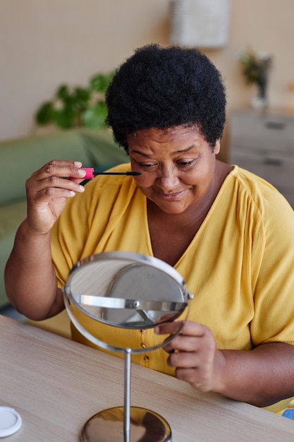 Abuela afroamericana con ropa informal maquillándose la cara