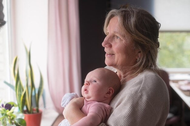 Abuela anciana sosteniendo a un recién nacido en sus brazos en casa