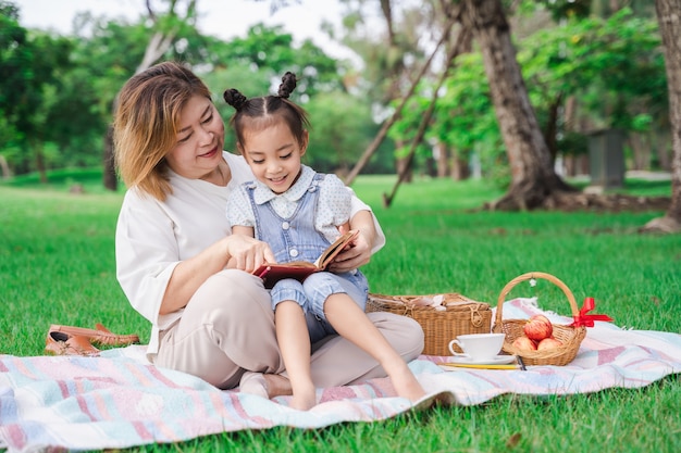 Abuela asiática y nieta que se sientan en el campo de cristal verde al aire libre, familia que disfruta de comida campestre junto en día de verano