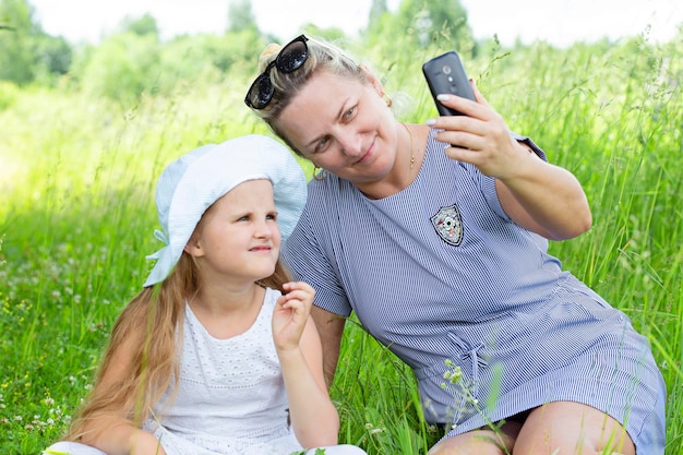 Abuela atractiva y linda nieta se sientan en el parque y toman una foto por teléfono