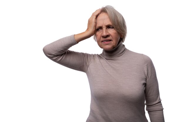 Abuela con cabello gris sosteniendo su cabeza contra un fondo con espacio de copia