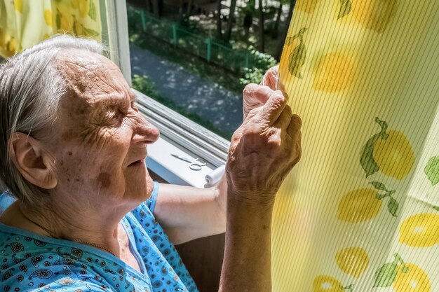 La abuela cose un agujero en la cortina del balcón de un edificio de apartamentos.