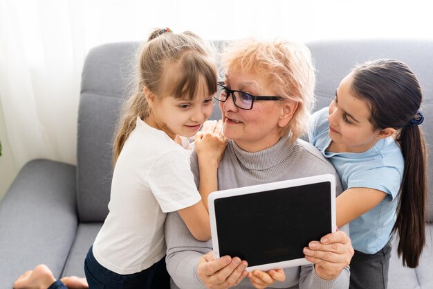 abuela y dos nietas usan una tableta en casa.