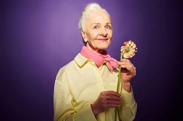 Abuela feliz con herbera fresca parada frente a la cámara