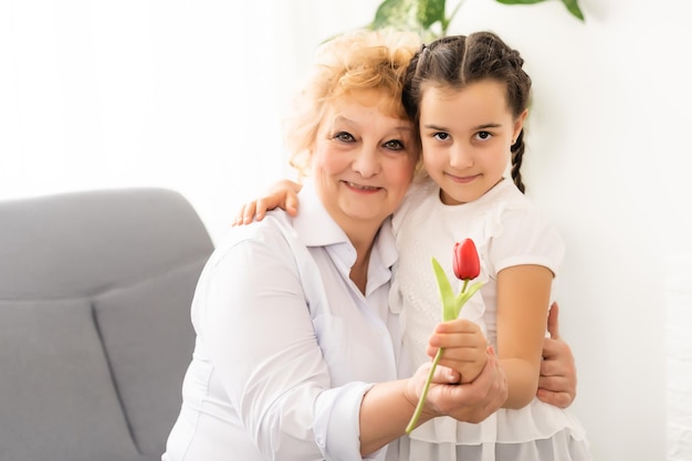 Abuela feliz con nieta. Mujer y niño con flor en casa.