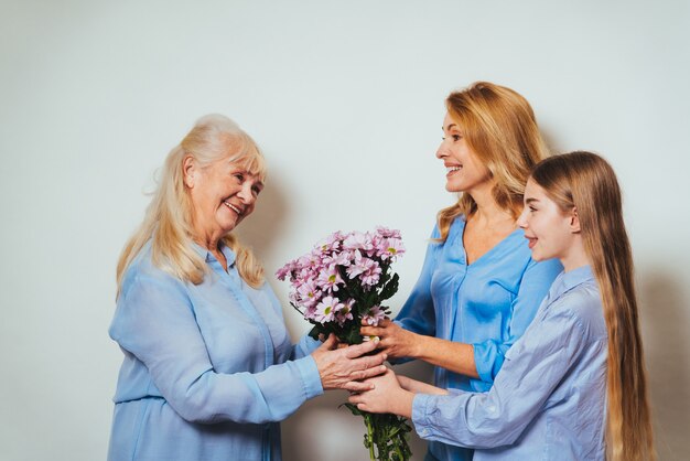 Abuela, hija y nieto juntos en casa dando ramo de flores