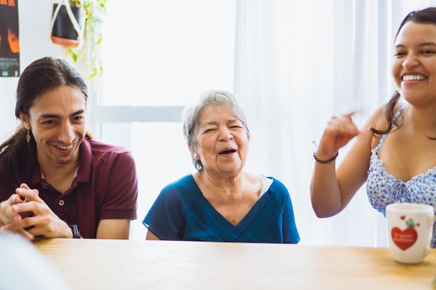 Abuela latina riéndose con sus nietos en el comedor en medio de una reunión familiar