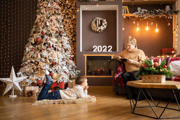 Abuela leyendo un libro a sus nietos cerca del árbol de navidad en casa en año nuevo