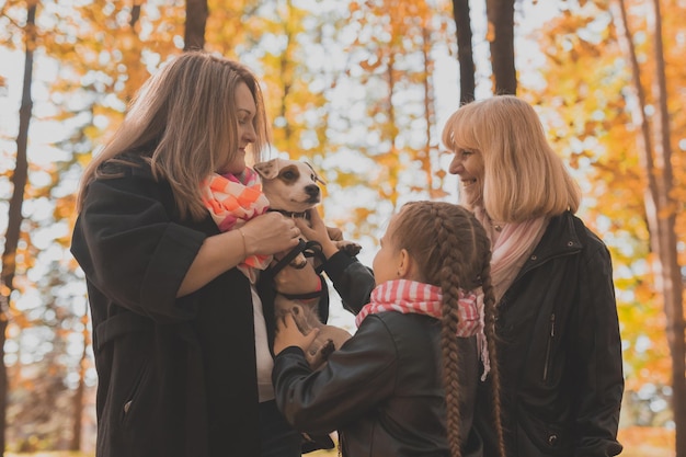 Abuela y madre con nieta divirtiéndose con el perro en el ocio de la generación de la temporada de otoño