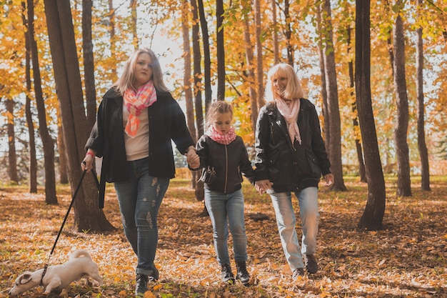 La abuela y la madre con la nieta vomitan hojas de otoño en el parque de otoño y se divierten. Concepto de generación, ocio y familia