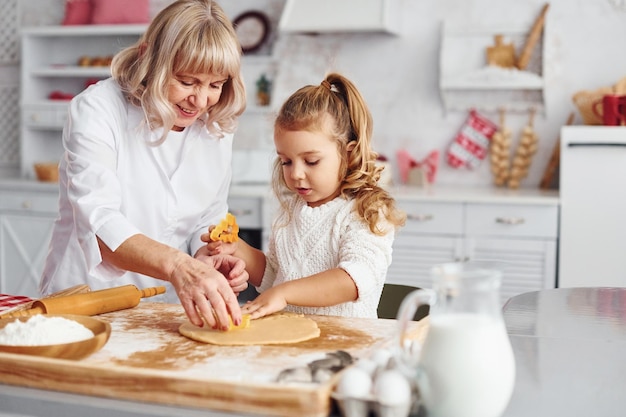 La abuela mayor con su nieta cocina dulces para Navidad en la cocina