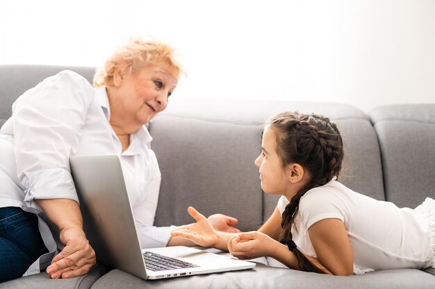 abuela moderna enseñando a su nieto cómo usar una computadora portátil en casa.