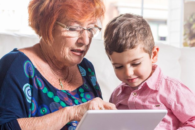 La abuela le muestra una tableta digital al niño en casa