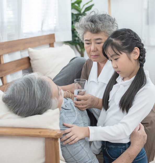 La abuela y la nieta asiáticas cuidan y cuidan, el abuelo le da un vaso de agua con medicamentos