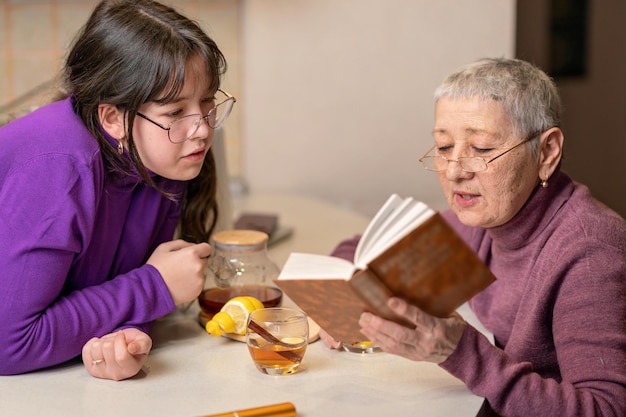 abuela y nieta beben té, se sientan a la mesa y leen un libro Enfoque selectivo