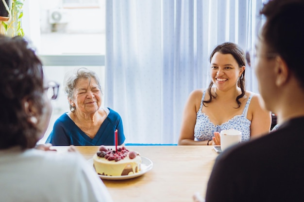 Abuela y nieta celebrando un cumpleaños con sus seres queridos frente a su pastel mientras cantan la canción de cumpleaños