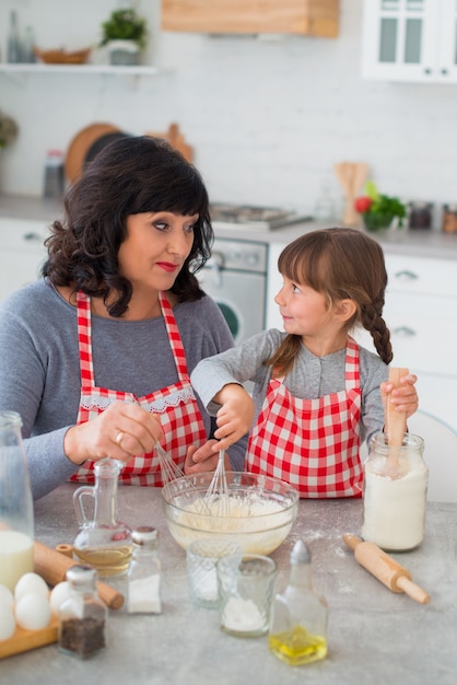 Abuela y nieta con delantales a cuadros cocinan en la cocina y se miran.