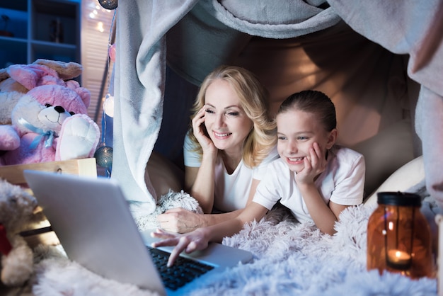 La abuela y la nieta están hablando con la familia en la computadora portátil en la casa combinada por la noche en casa.