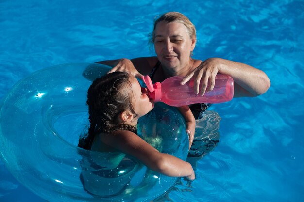 Abuela y nieta en la piscina una joven abuela le da a su nieta agua de un r ...