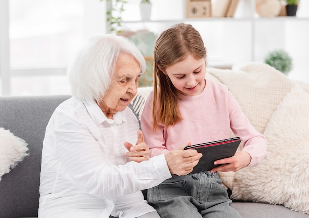 Abuela y nieta sentadas en el sofá y mirando la tableta juntos