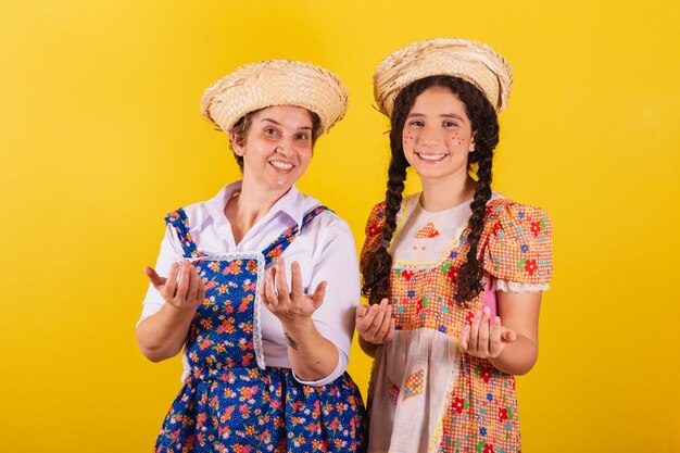 Abuela y nieta vestidas con ropa típica de Festa Junina Llamando con las manos invitando a venir aquí