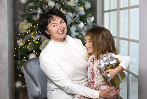 Abuela con una niña en el fondo de adornos navideños y una ventana grande