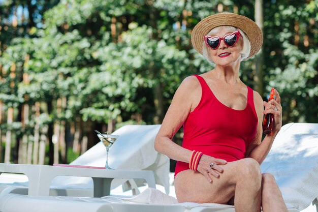 Abuela de pelo rubio con elegantes accesorios mientras está sentada en la tumbona esperando marido