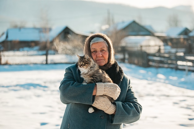 Abuela rusa, sostiene un gatito en sus brazos, pueblo, Siberia, invierno.