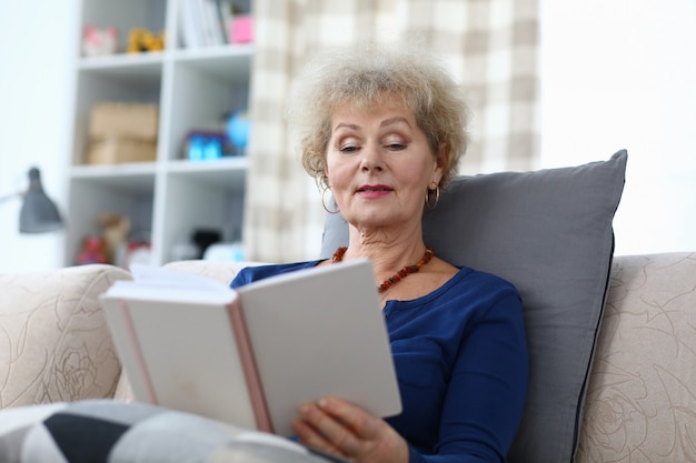 La abuela se sienta en casa y lee con entusiasmo.