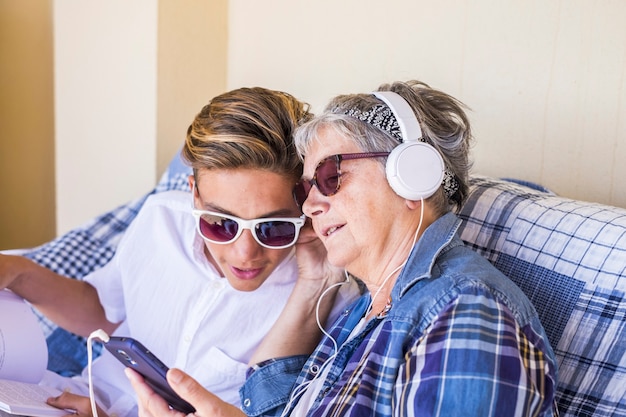 Abuela y sobrino adolescente pasaron tiempo juntos al aire libre en la terraza de casa escuchando música con el moderno teléfono inteligente y auricular