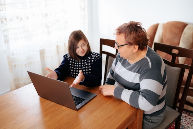 Una abuela y su pequeña nieta están estudiando juntos en casa usando su portátil para investigar