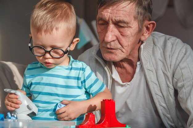 Foto abuelo anciano juega con su nieto con bloques de plástico