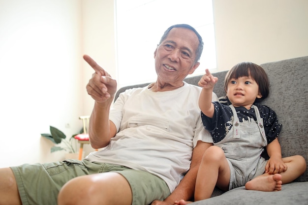 Abuelo asiático viendo televisión con su nieta en el sofá de la sala