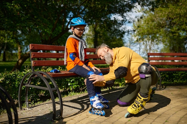 Abuelo ayudando a su nieto a ponerse patines en un parque urbano