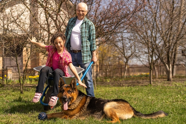 Abuelo cargando a su nieta en una carretilla en un parque.