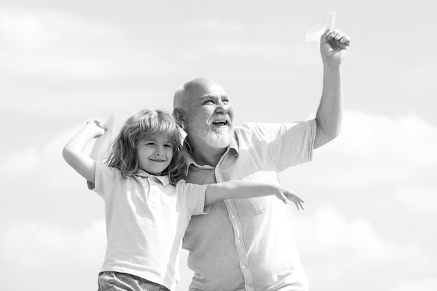 Abuelo e hijo jugando con avión de papel de juguete contra el fondo del cielo de verano niño niño con sueños...