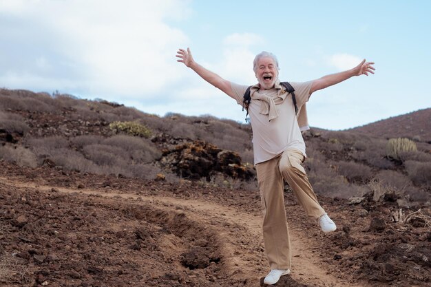 Abuelo emocionado loco saltando en una excursión al aire libre levantando una pierna con los brazos abiertos Hombre barbudo mayor disfrutando de la vida y la jubilación